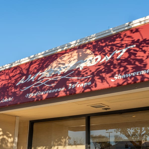 Red awning with "Waterfront Mediterranean Wraps" and "Shawerma" text, casting tree shadows.