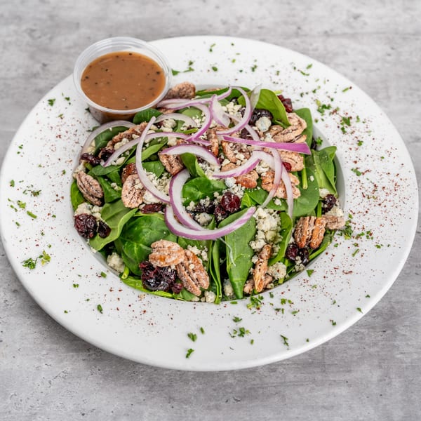 Spinach salad with red onions, pecans, dried cranberries, blue cheese, and a side of dressing.