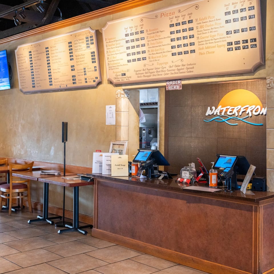 The interior of Waterfront Pizza shows a menu board, ordering counter, and dining tables.