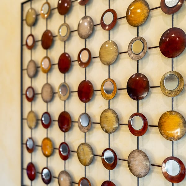Decorative wall art with a grid of metallic circles in red, gold, and silver, some with mirrors.