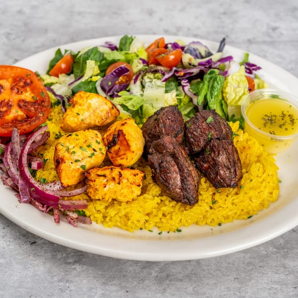 Grilled chicken and beef skewers with yellow rice, salad, grilled tomato, red onions, and dressing.