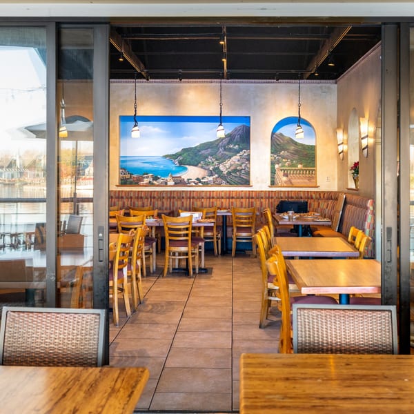 Waterfront Pizza's dining room with wooden tables and chairs, and a large mural of a coastal town.