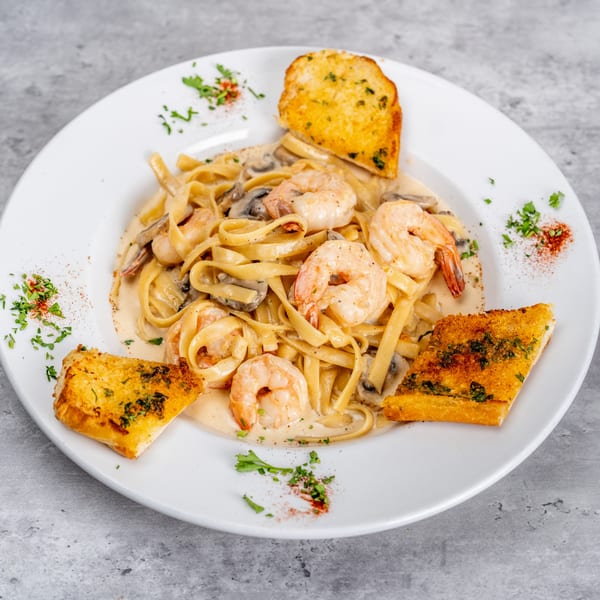Creamy shrimp fettuccine pasta with mushrooms, garnished with parsley and paprika, served with garlic bread.