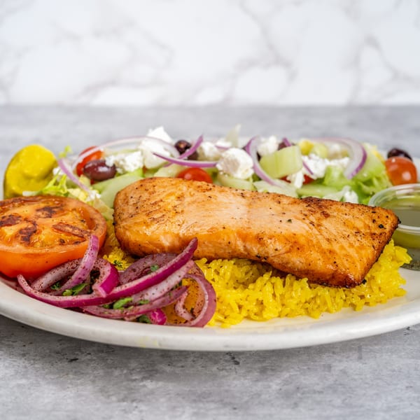 Grilled salmon fillet on yellow rice with a side of Greek salad and grilled tomato.