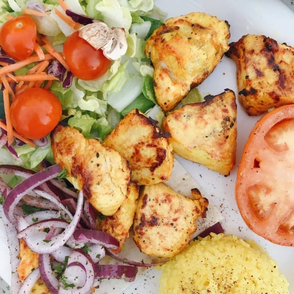 Grilled chicken pieces with a side salad, sliced red onions, a tomato slice, and yellow rice.