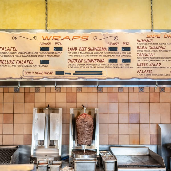 A menu board above a shawarma spit and grill in a restaurant kitchen.