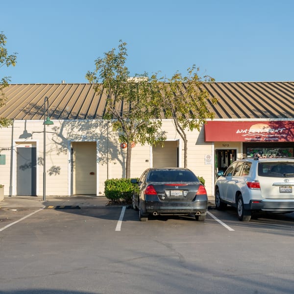 Exterior of Waterfront Pizza, a Mediterranean restaurant with a red awning and parked cars.