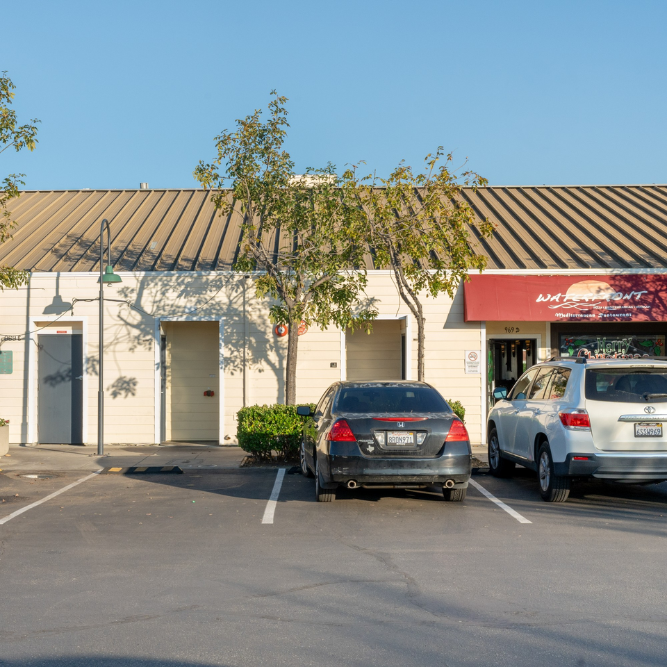 Exterior of Waterfront Pizza, a Mediterranean restaurant with a red awning and parked cars.