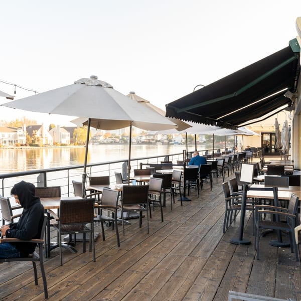 Waterfront Pizza's outdoor patio with tables, umbrellas, and diners overlooking a lake with houses.